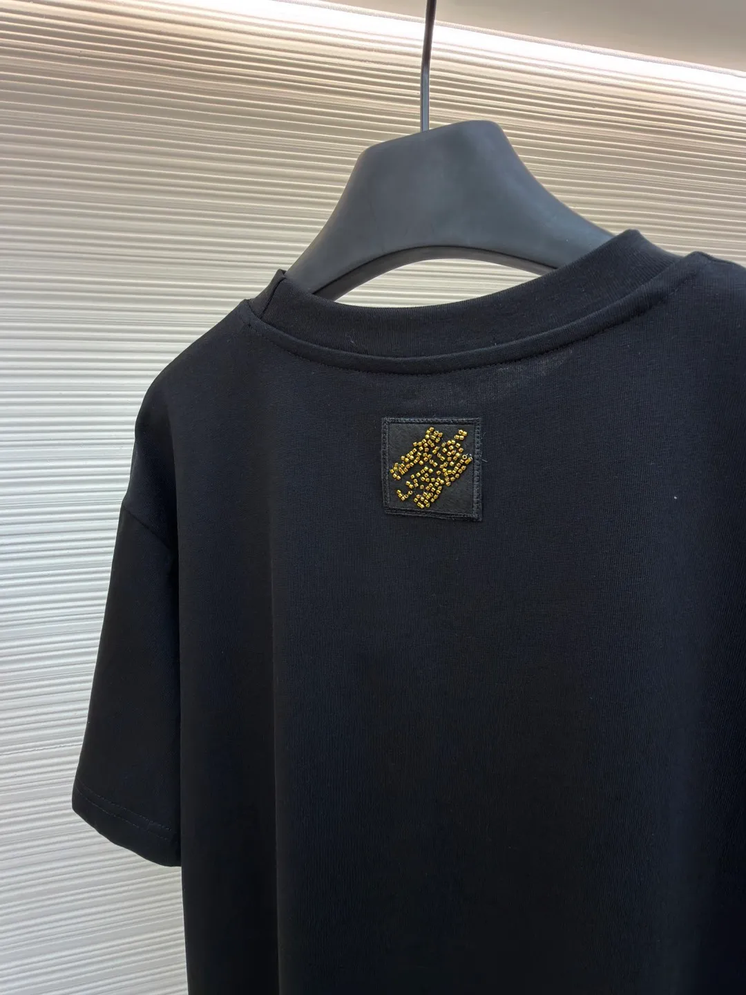 LOUIS VUITTON cotton round neck embroidered Vuitton signature logo short sleeves ●Original version: purchased and developed for 12300 ●Item number: 1682273-A10 ●Fabric: cotton fabric ●Technology: embroidery production ●Color: black ●Version: fitted version ●Weight: about 295 grams ●Size: S-M-L-XL ●Description: This white short-sleeved T-shirt is made of high-count combed cotton fabric and has been treated with pre-washing technology. It has a soft and skin-friendly touch and is not easy to deform. The silhouette of the shirt is a loose shoulder design, which meets the needs of modern casual wear. The core decoration area on the chest uses hand-beading and bronzing technology, and uses metallic gold sequins and embroidery threads intertwined to outline a three-dimensional letter pattern. The sequins are layered and inlaid, and each one is manually positioned and fixed by craftsmen to ensure a regular texture and uniform gloss. The edges of the letters are sewn with matte silk thread to form a visual contrast between gold and matte, while reinforcing the decorative structure to avoid falling off during wear. The neckline uses double-needle hemming technology and is matched with ribbed cuffs of the same fabric. It is durable and fits the neck. The overall craftsmanship combines handicraftsmanship with modern clothing technology, and the details show exquisite texture. The overall wiring is straight and delicate, the fabric is comfortable and soft, and the color is consistent without color difference. It can be matched with the same style to create a fashionable look and control various occasions. Customized accessories, complete with three standards, same style for men and women!